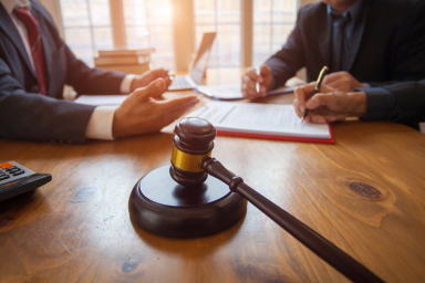 Un marteau de juge avec son socle et trois personnes autour d’une table